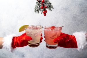 Two hands with red and white festive gloves holding cocktails in cheers position