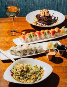 Plates of sushi, sweet cakes and a glass of wine