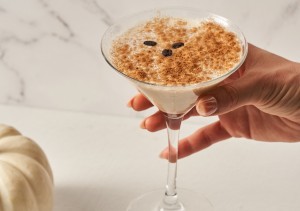 Hand holding a pumpkin mocha martini with a white pumpkin in the background