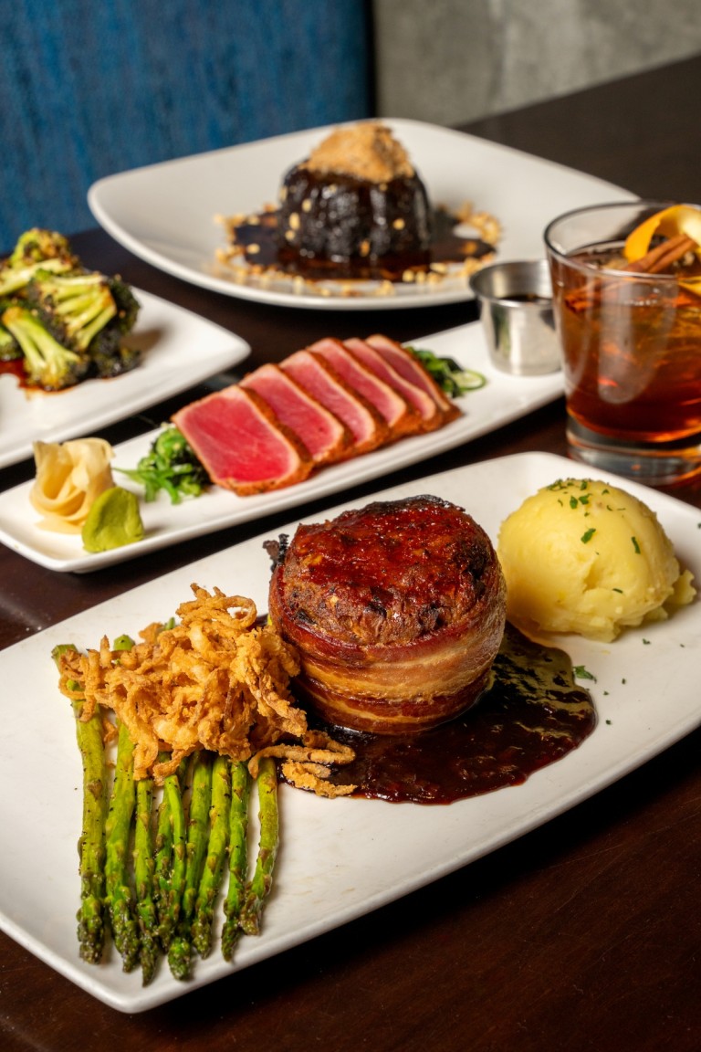 a restaurant table spread featuring several plated dishes and a cocktail.